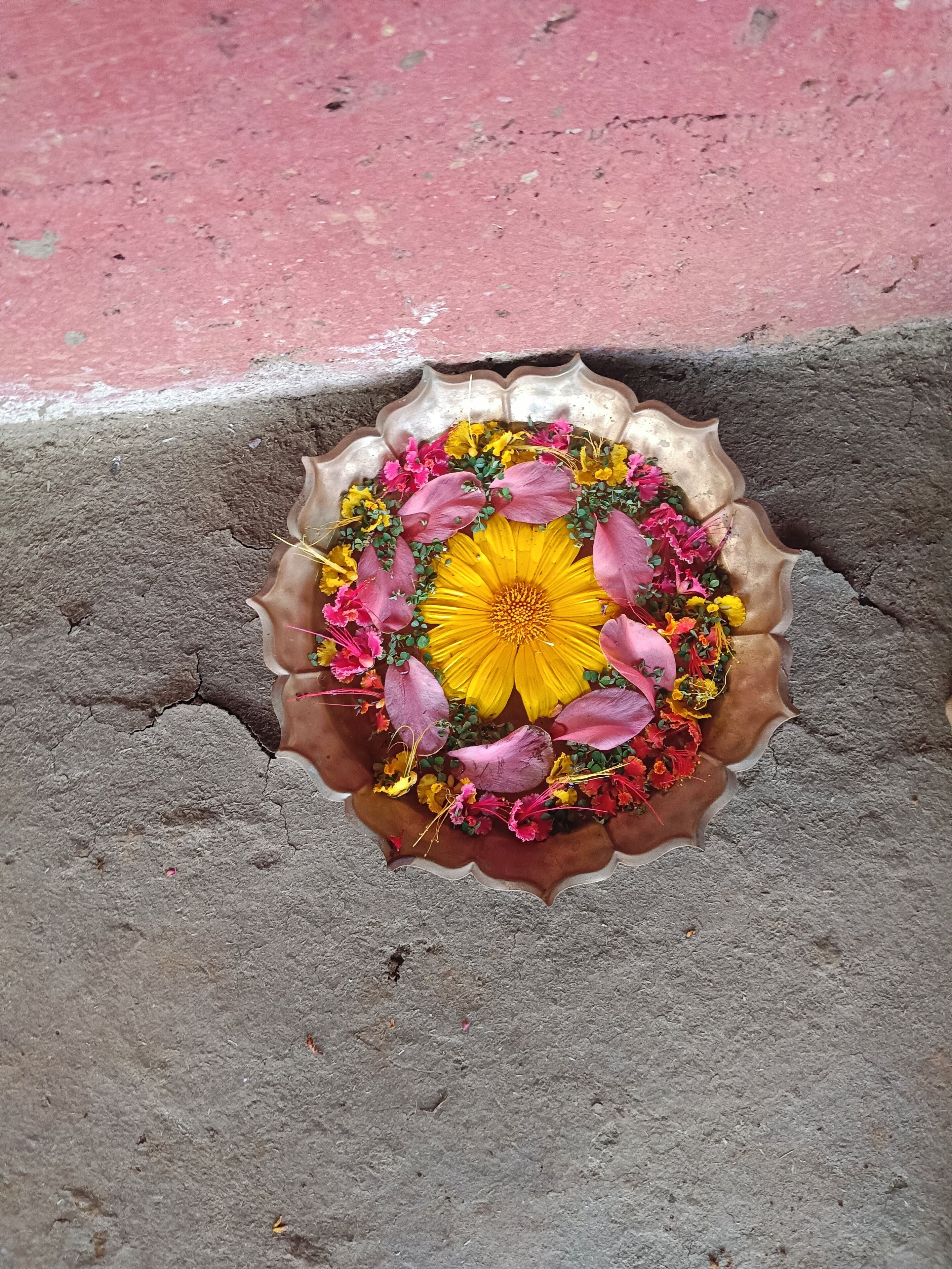 Um arranjo de flores numa taça de metal com borda ondulada, sobre uma superfície de concreto.
