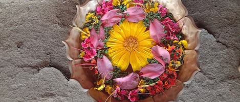 Um arranjo de flores numa taça de metal com borda ondulada, sobre uma superfície de concreto.