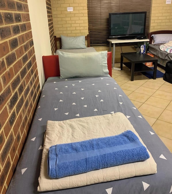 A single bed with a grey and white patterned bedspread, a blue towel, and two pillows. - Enjoyable 1-bedroom house with AC in charming Heathridge (Heathridge)