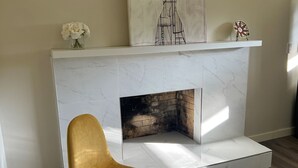Un salón moderno con chimenea blanca, un sillón dorado y una obra de arte con motivos de ciervo sobre la repisa.