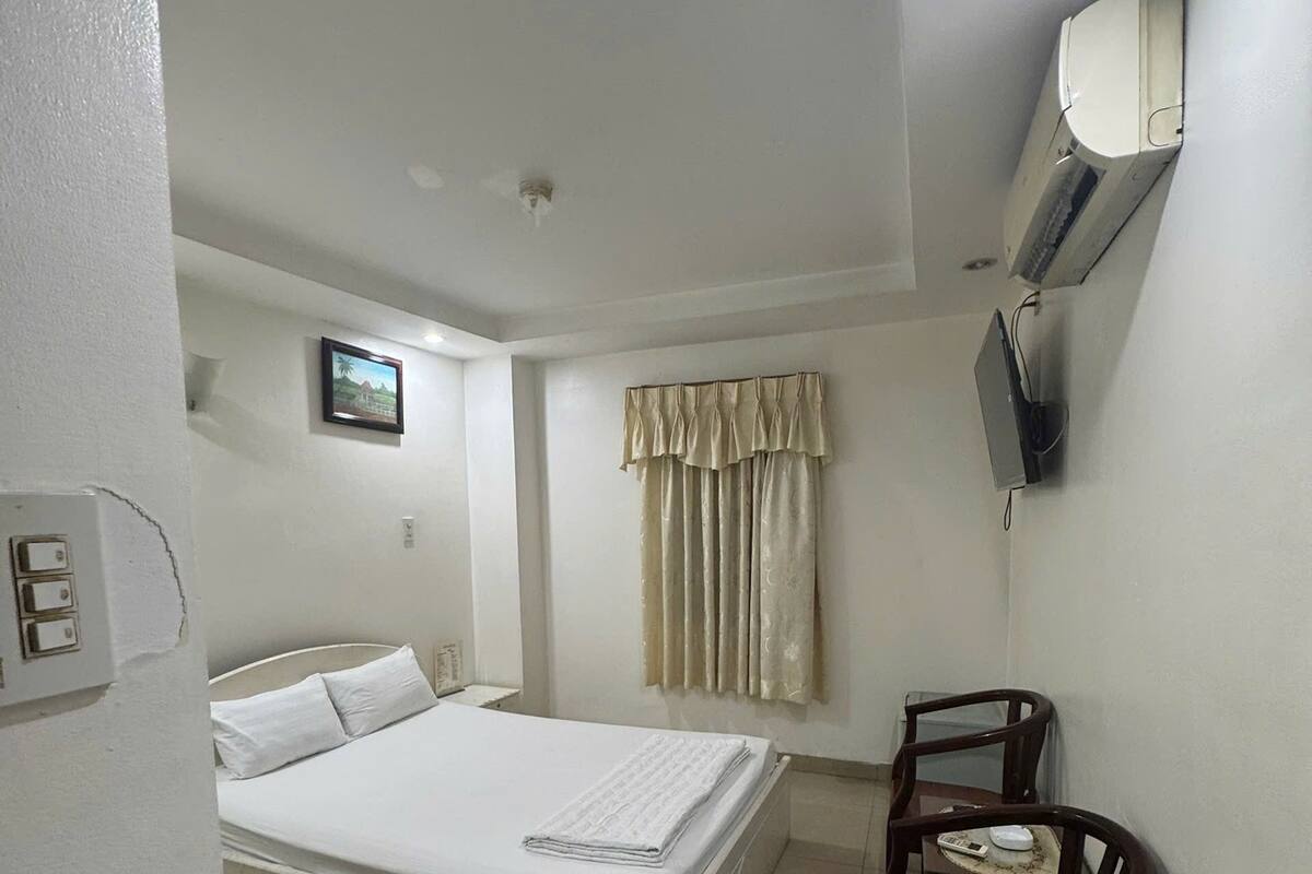 Una habitación de hotel con una cama, una silla, un escritorio, un televisor y un ventanal con cortinas.