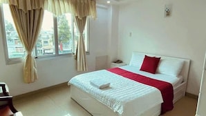A neatly made bed with a white and red bedspread, a nightstand with a lamp, and a window with curtains. - SEVEN STARS HOTEL  (Ho Chi Minh City)