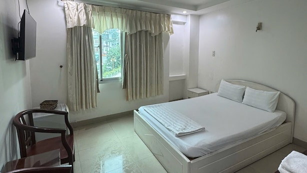 A hotel room with a bed, a chair, a TV, and a window with curtains. - SEVEN STARS HOTEL  (Ho Chi Minh City)