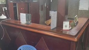 A reception desk with a wooden finish, two blue plastic chairs in front, and a wall-mounted information board. - SEVEN STARS HOTEL  (Ho Chi Minh City)