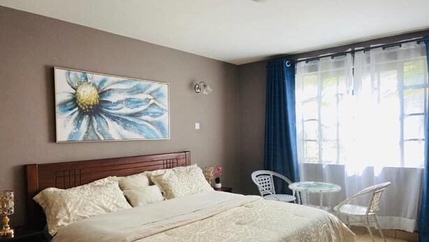 Une chambre à coucher comprenant un lit, une table de chevet, une lampe, une chaise, une petite table et une fenêtre avec des rideaux.
