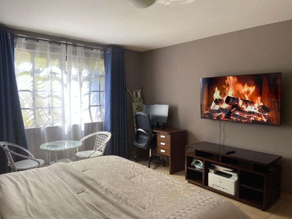 Quarto de hotel com cama, escrivaninha, cadeira, televisão e janela com cortinas.