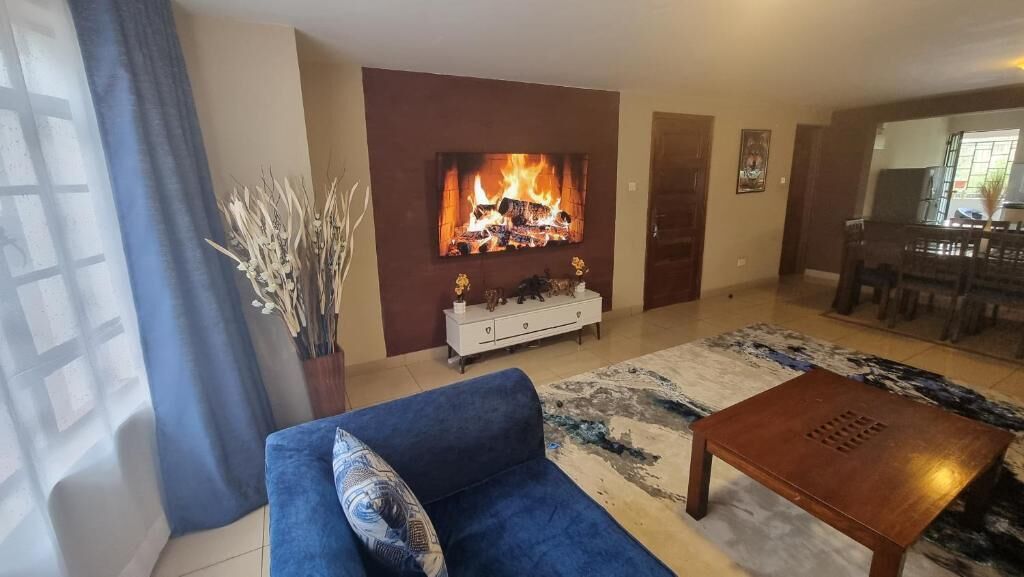 Una sala de estar con un sofá azul, una mesa de centro, una chimenea y un comedor con una mesa y sillas de madera.