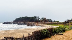A beach with a rocky shoreline, a temple, and a path leading to the temple. - Sea Breeze Beach Resort (Mahabalipuram)