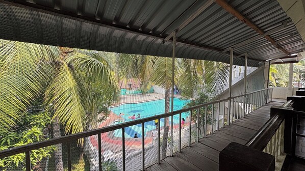A covered outdoor area with a pool, surrounded by palm trees and a mesh fence. - Sea Breeze Beach Resort (Mahabalipuram)