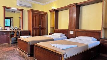 Une chambre d’hôtel avec deux lits simples, des armoires en bois, un bureau avec une chaise et un appareil de climatisation.