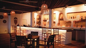A cozy bar area with wooden furniture, a central bar counter, and unique wall shelves displaying bottles. - Sea Breeze Beach Resort (Mahabalipuram)