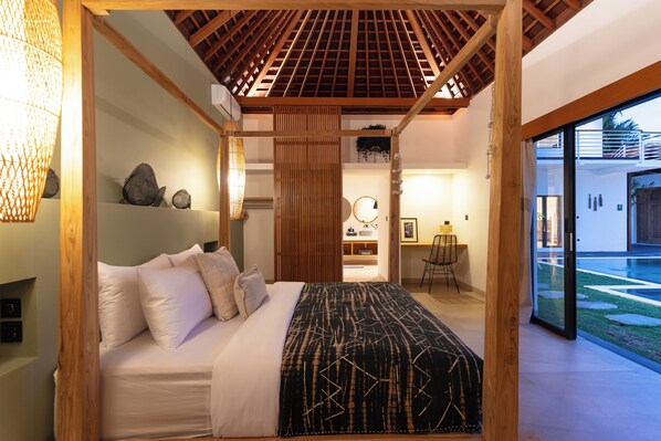 Una camera da letto moderna con soffitto in legno, un letto grande con biancheria da letto bianca e vista su un giardino attraverso una porta in vetro.
