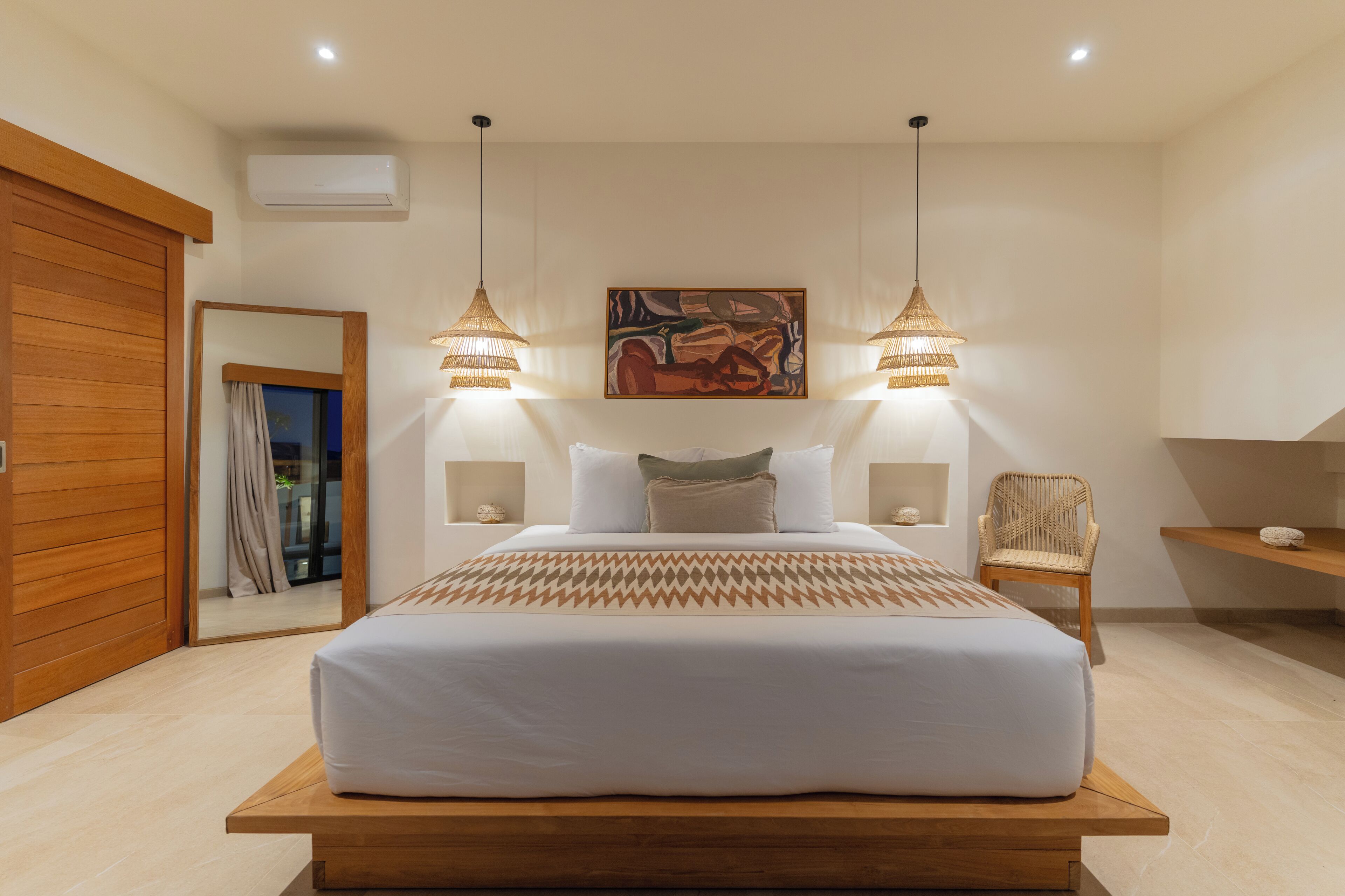 A modern bedroom with a large bed, two bedside lamps, a wall-mounted air conditioner, and a wooden floor.
