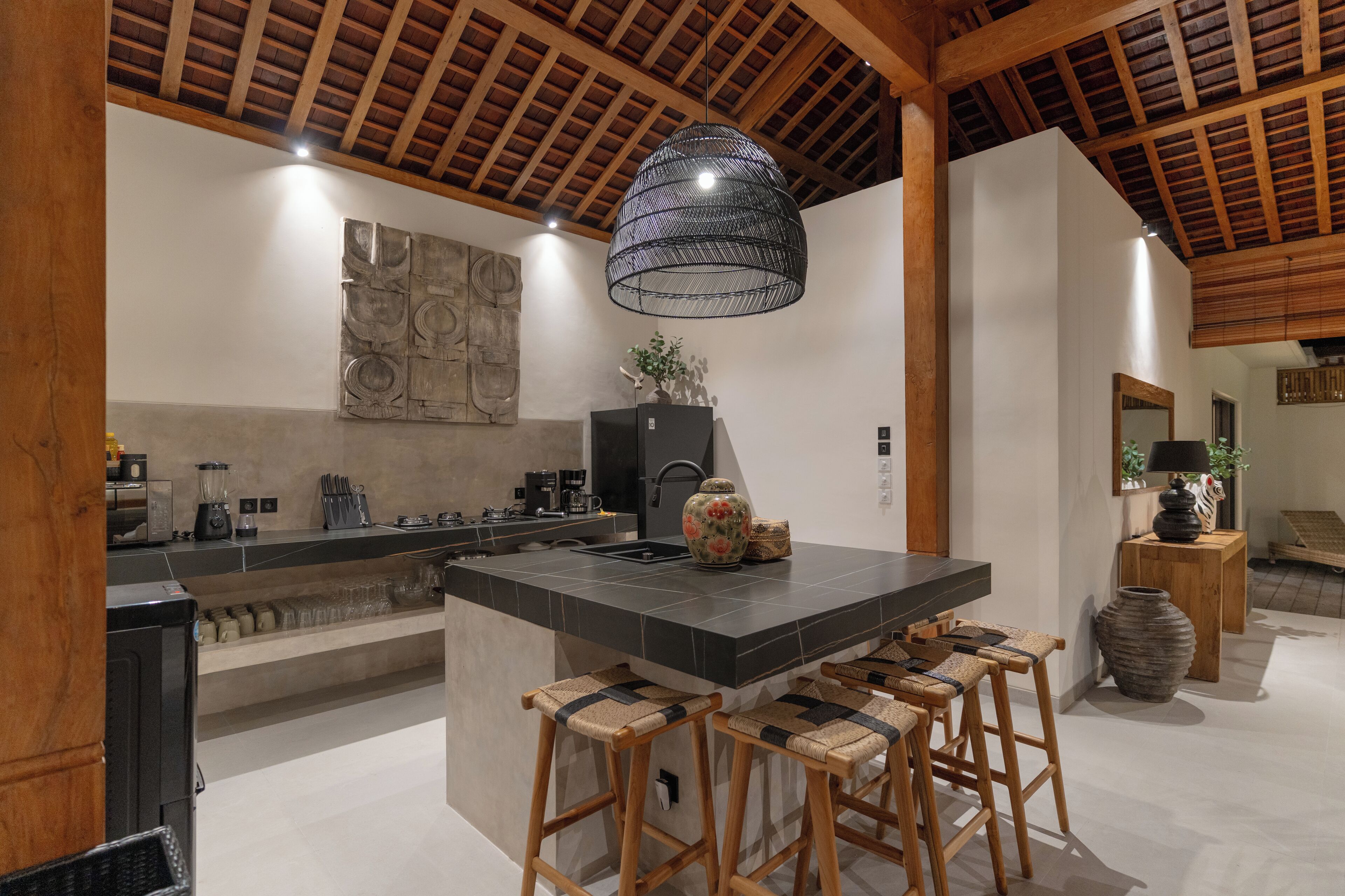 A modern kitchen with a large island, bar stools, a hanging light fixture, and a rustic ceiling.