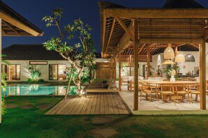 A well-lit outdoor area with a pool, wooden deck, and a covered seating area with tables and chairs. - Villa Nador by Alfred in Bali (Seminyak)