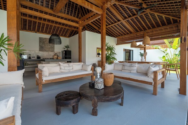 A spacious living area with wooden furniture, a round coffee table, and a kitchen in the background. - Villa Nador by Alfred in Bali (Seminyak)