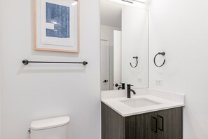 Une salle de bain moderne avec des toilettes blanches, un lavabo avec un meuble sombre et un tableau encadré au mur.