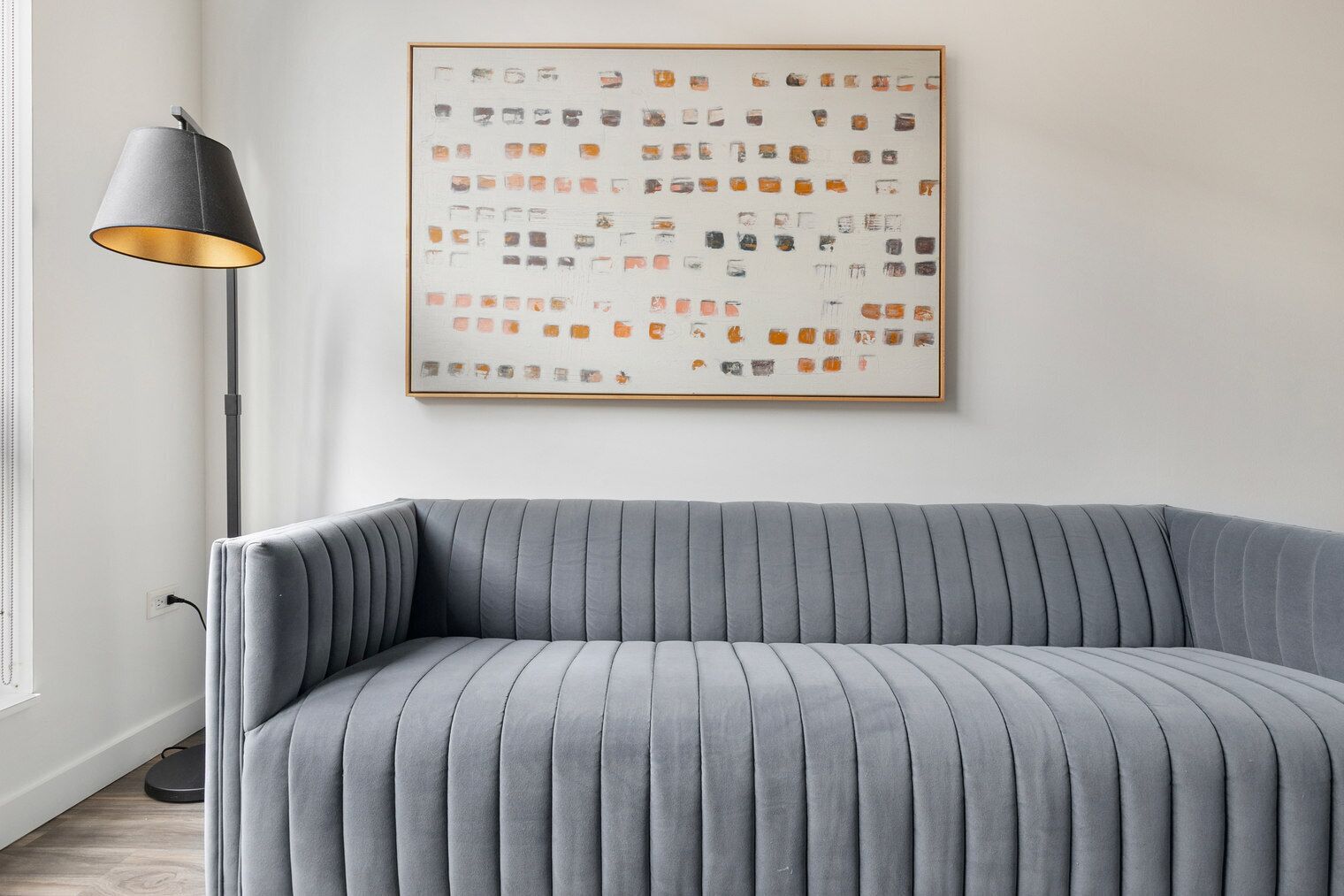 A modern living room with a grey upholstered sofa, a floor lamp, and a framed abstract artwork on the wall.