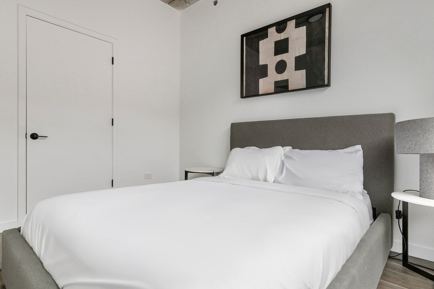 Een moderne slaapkamer met een groot bed, een nachtkastje en een wanddecoratie met abstracte kunst.