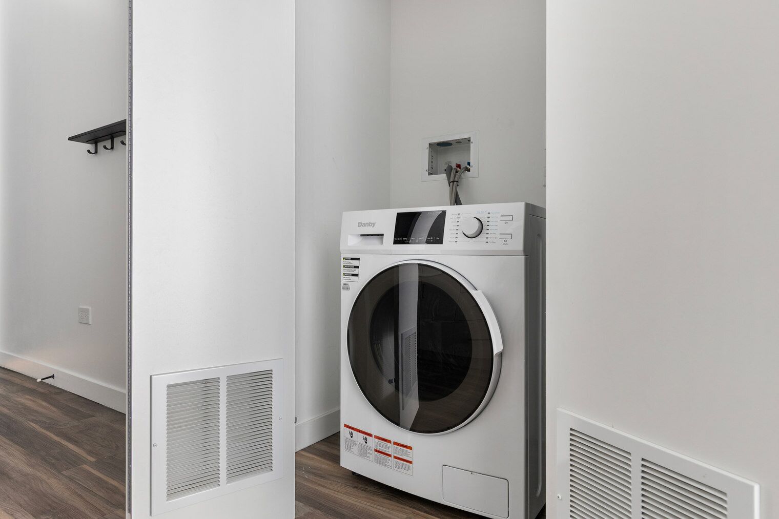 A laundry room with a front-loading washing machine, a vent, and a small electrical panel on the wall.
