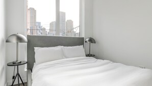 Ein modernes Hotelzimmer mit einem großen Bett, zwei Nachttischlampen und Blick auf die Stadt durch das Fenster.