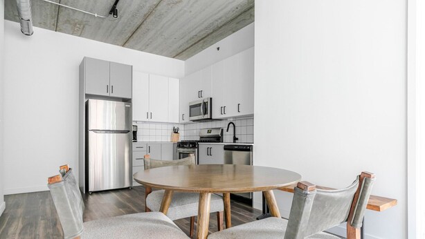 Eine moderne Küche mit weißen Schränken, Edelstahlgeräten und einem runden Holztisch mit vier Stühlen.