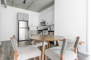 Une cuisine moderne avec des meubles blancs, des appareils en acier inoxydable et une table ronde en bois, accompagnée de quatre chaises.