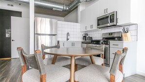 A modern kitchen with white cabinets, stainless steel appliances, and a round wooden table with grey upholstered chairs. - Blueground | Near North Side, rooftop, nr Riverwalk (Chicago)