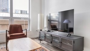 A modern living room with a large flat-screen TV, a cushioned chair, a small table, and a large window offering a city view. - Blueground | Near North Side, rooftop, nr Chicago River (Chicago)