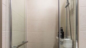 Eine gläserne Duschkabine mit Handbrause und einer kleinen Ablage für Toilettenartikel.