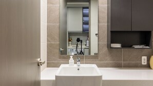 Ein modernes Badezimmer mit einem weißen Waschbecken, einem Spiegel und einem dunkel gefliesten Boden.