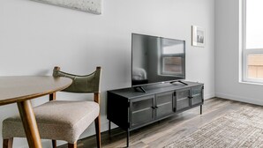 Ein modernes Wohnzimmer mit Flachbildfernseher auf einem schwarzen Schrank, einem runden Holztisch und einem grünen Polsterstuhl.