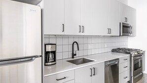 Eine moderne Küche mit weißen Schränken, einem Edelstahlkühlschrank, einer Kaffeemaschine, einer Spüle, einer Mikrowelle und einem Herd.