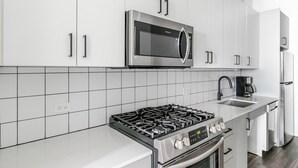 Eine moderne Küche mit weißen Schränken, einer Edelstahl-Mikrowelle, einem Gasherd und einem eingebauten Backofen.