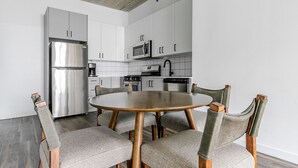 Eine moderne Küche mit weißen Schränken, Edelstahlgeräten und einem runden Holztisch mit gepolsterten Stühlen.