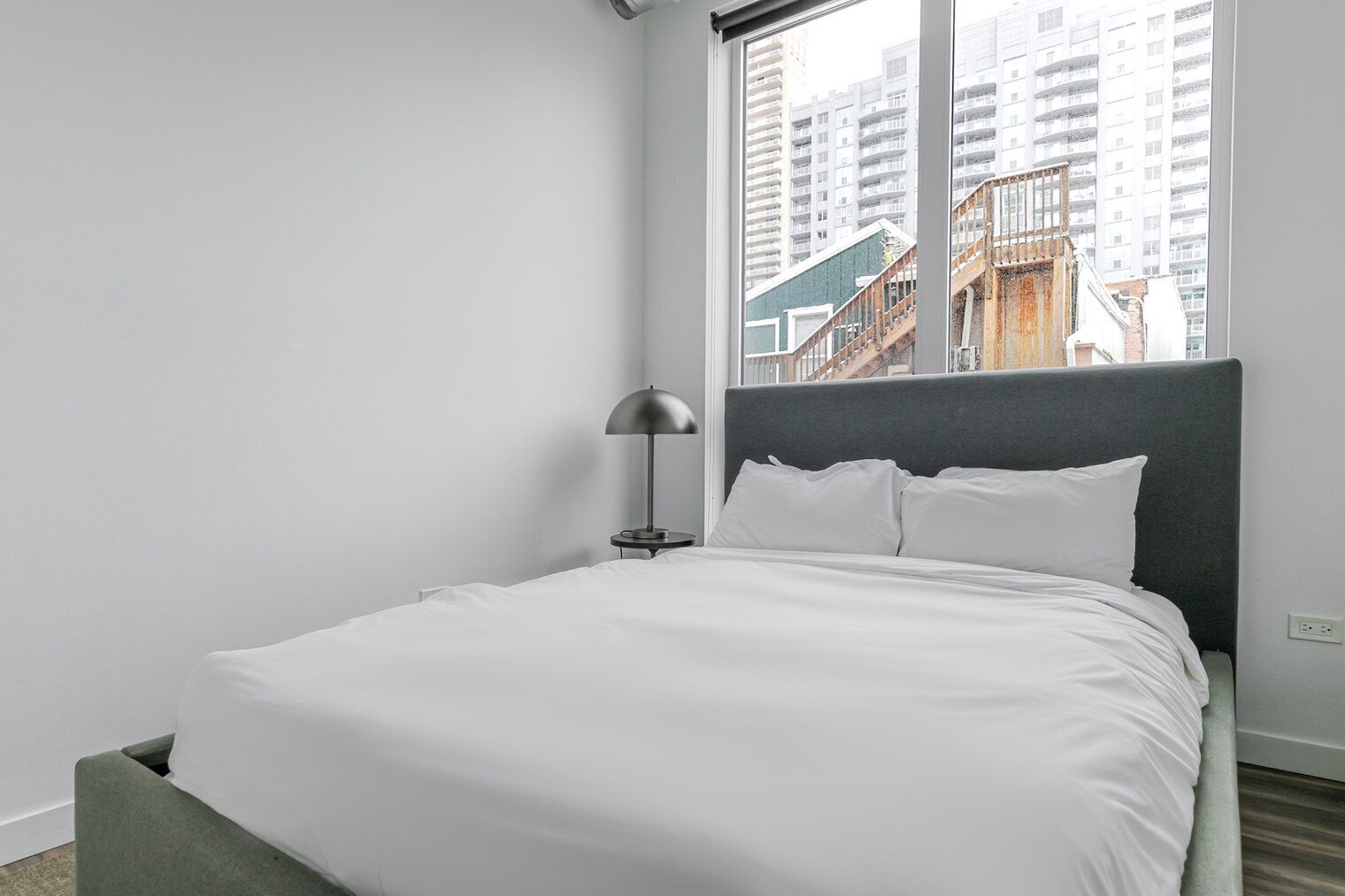 A modern hotel room with a large bed, a bedside table, and a window with a city view.