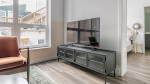 Ett modernt vardagsrum med ett stort fönster, en soffa, en tv som står på ett skåp och ett litet bord med en lampa.