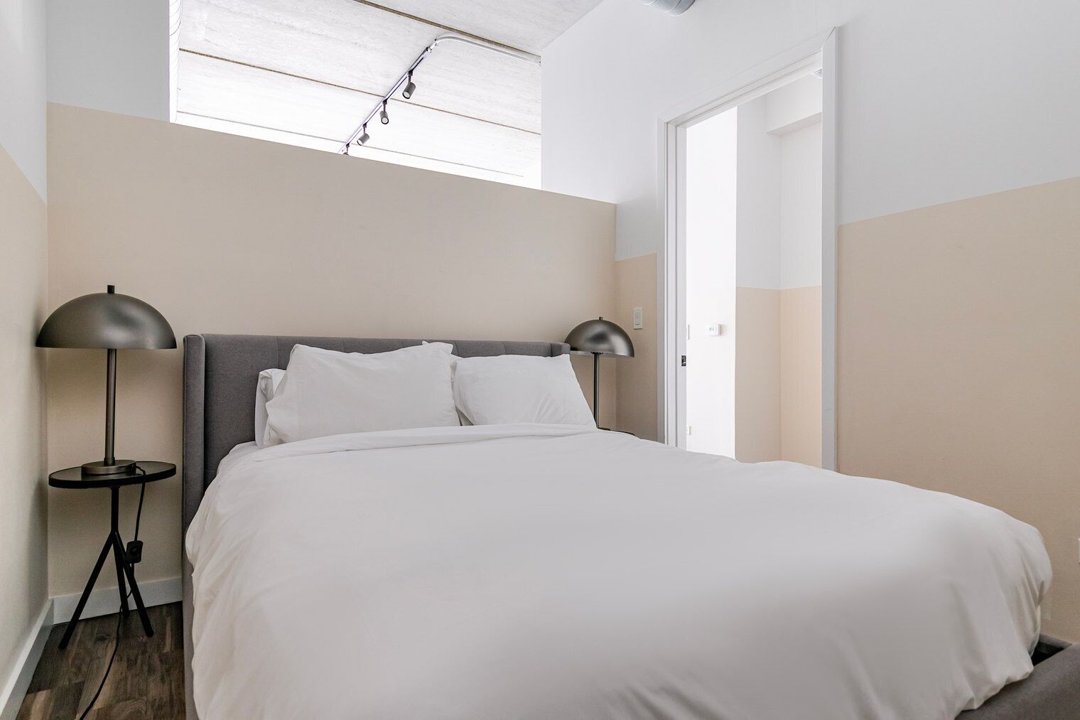 A neatly made bed with white bedding, a grey headboard, and two black floor lamps on either side.