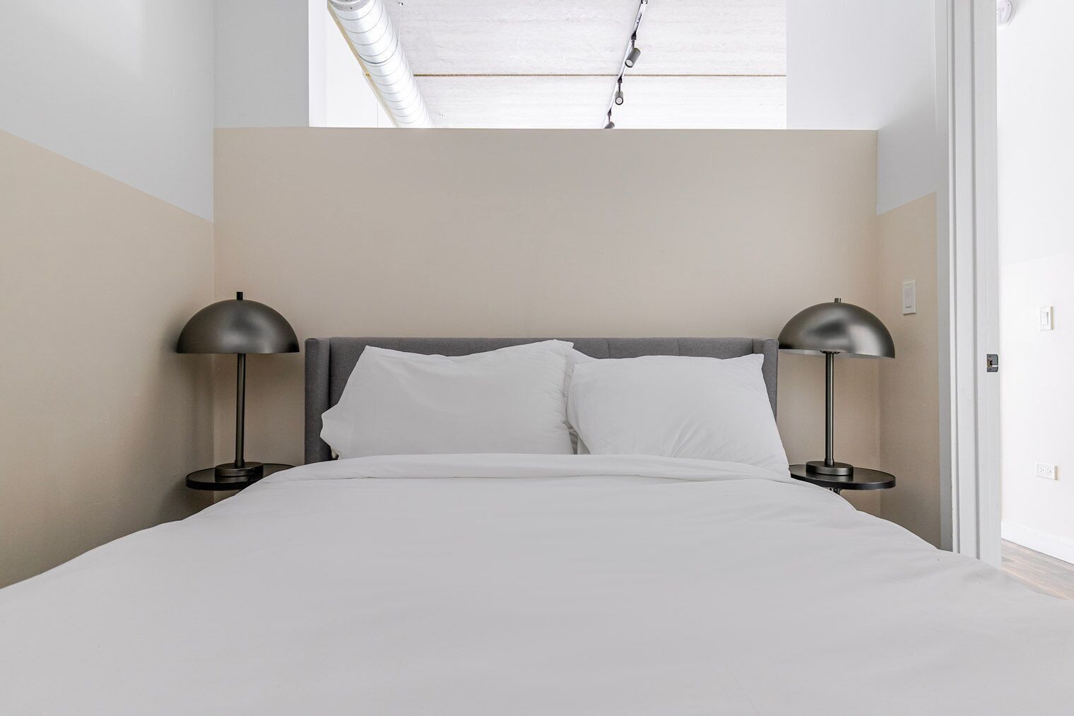 A modern bedroom with a bed, two bedside lamps, and a skylight.