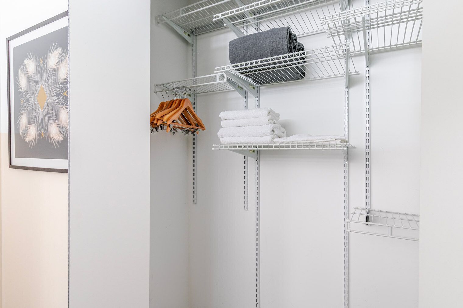 Ein weißer Schrank mit Metallregalen, gefüllt mit gefalteten Handtüchern und einem aufgerollten grauen Handtuch.