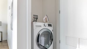 A compact, white laundry room with a front-loading washer and dryer, a small shelf with a tissue box, and a vent on the wall. - Blueground | Near North Side, rooftop, nr Chicago River (Chicago)
