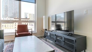 A modern living room with a large flat-screen TV, a sofa, a coffee table, and a view of a cityscape through large windows. - Blueground | Near North Side, rooftop, nr Riverwalk (Chicago)