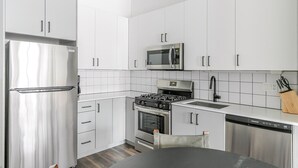 Een moderne keuken met witte kastjes, roestvrijstalen apparatuur, een gasfornuis, een magnetron en een vaatwasser.