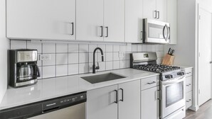 Een moderne keuken met witte kasten, een roestvrijstalen spoelbak, een koffiezetapparaat, een magnetron en een fornuis.