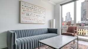 Een moderne woonkamer met een grijze bank, een salontafel en een groot raam met uitzicht op de stad.