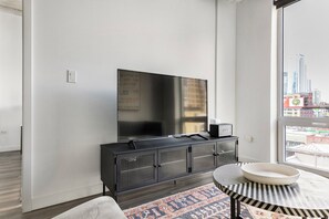 A modern living room with a large flat-screen TV mounted on a wall, a black entertainment unit with a speaker, a round coffee table with a white bowl, and a patterned rug. - Blueground | Near North Side, rooftop, nr Riverwalk (Chicago)