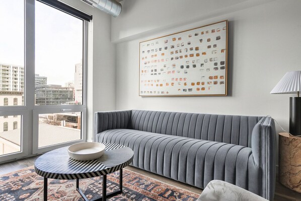 A modern living room with a grey sofa, a round coffee table with a black and white striped top, and a large abstract painting on the wall. - Blueground | Near North Side, rooftop, nr Riverwalk (Chicago)