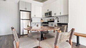 Une cuisine moderne avec des meubles blancs, des appareils en acier inoxydable et une table ronde en marbre, accompagnée de quatre chaises.