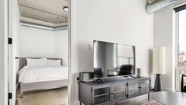 Une chambre d’hôtel avec un lit, un téléviseur posé sur une commode, une lampe et une vue sur la ville par la fenêtre.