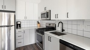 Une cuisine moderne dotée d’appareils électroménagers en acier inoxydable, de meubles blancs et d’un robinet noir.